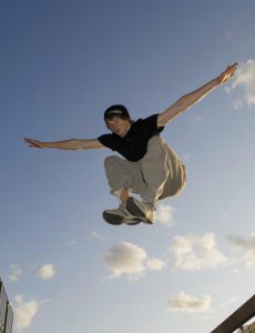 Parkour practioner jumping down (performing a drop). His appears to be flapping his arms like wings.