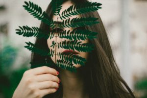 Beautiful brunette women hiding behind a green branch with lots of leafs she holds in her hand