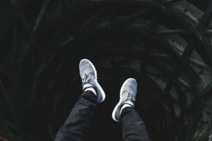 Man sitting above a black hole built in the ground. We only see his knees, feet and sneakers dangling above the abyss.